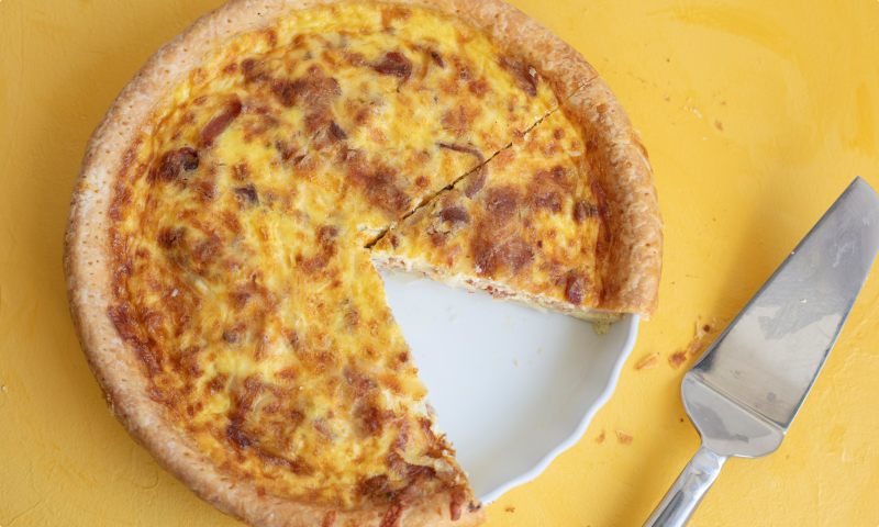 quiche Lorraine from elephants delicatessen on a a yellow table with one slice cut out of it