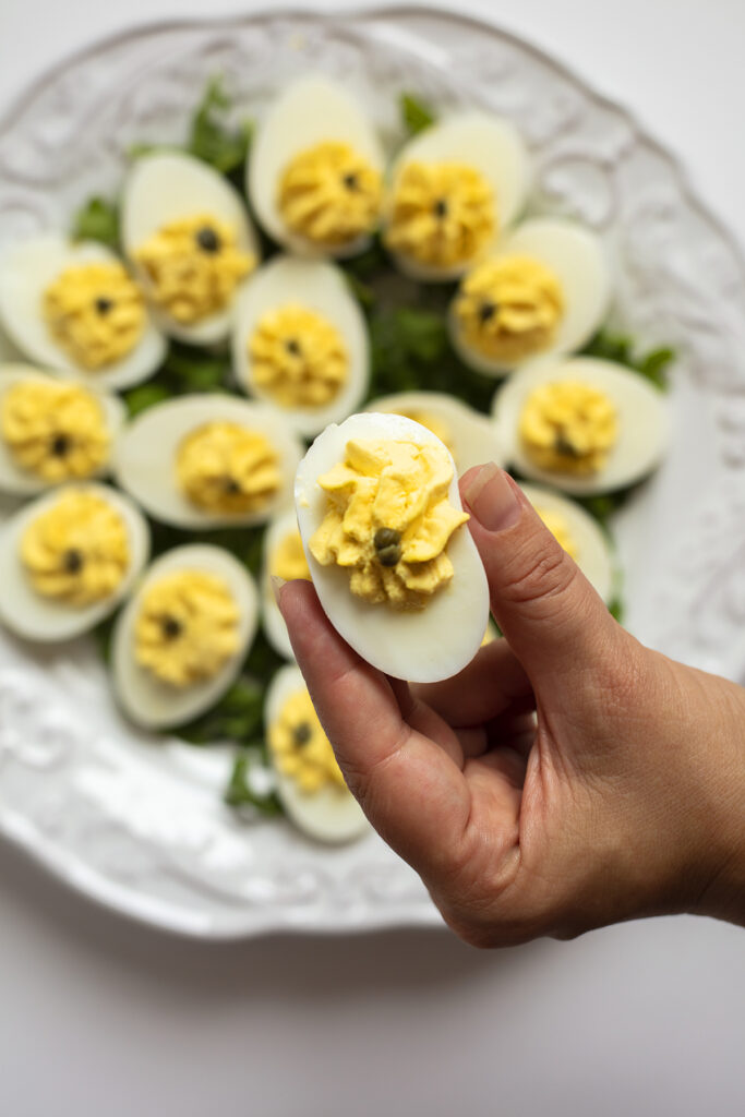 Someone holding a deviled egg above a tray full of more deviled eggs